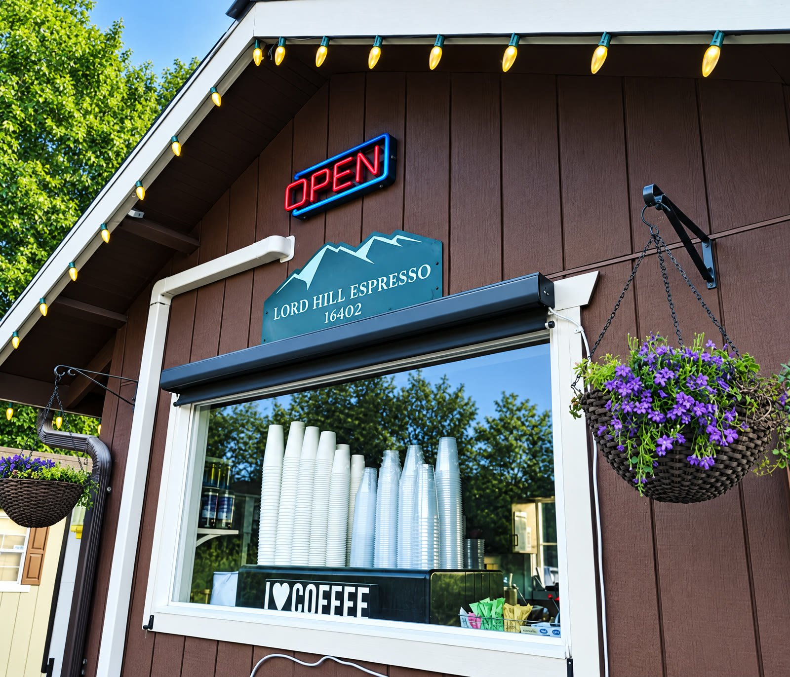 The Lord Hill Espresso drive-through window with the OPEN sign, the mountain sign and a hanging basket of purple flowers